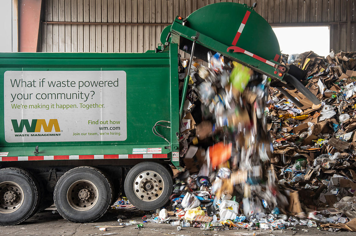 A green Waste Management truck dumping its waste